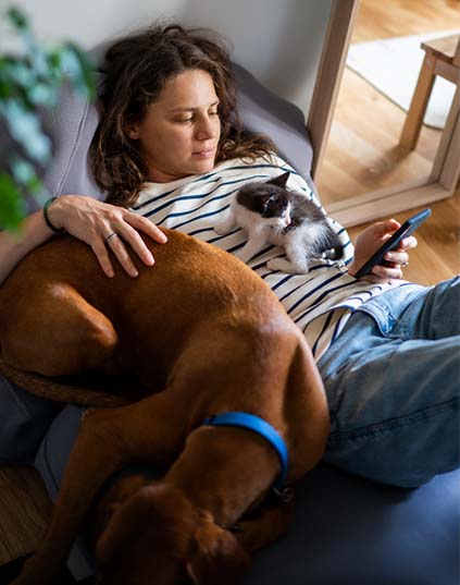 A woman relaxing on a sofa with her dog and cat